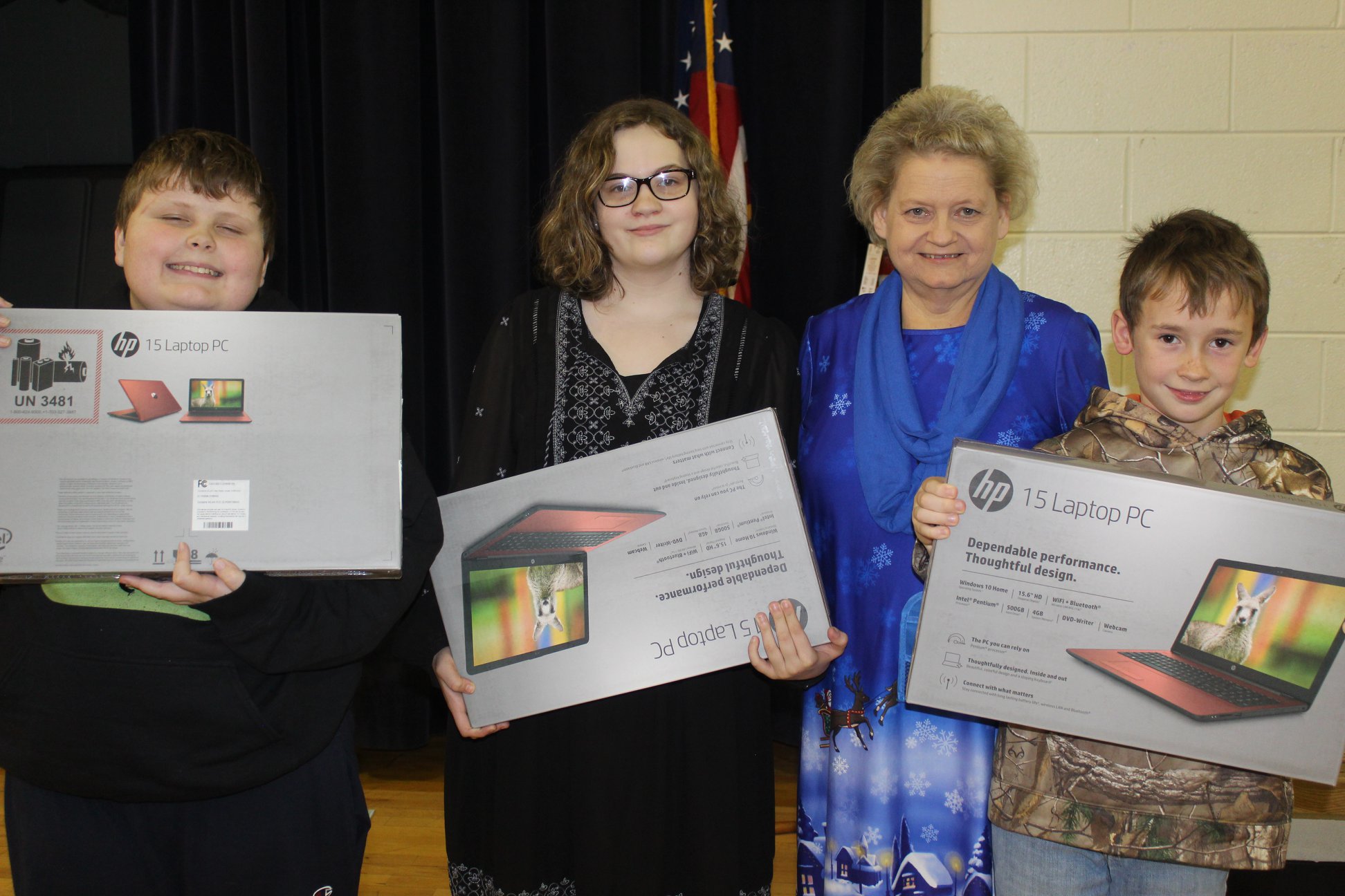 Three students and a teacher smile while holding new laptops received through Americans Helping Americans® classroom grants.