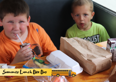 Two boys enjoy healthy lunches and milk inside a retired school bus converted for the Summer Lunch Box program.