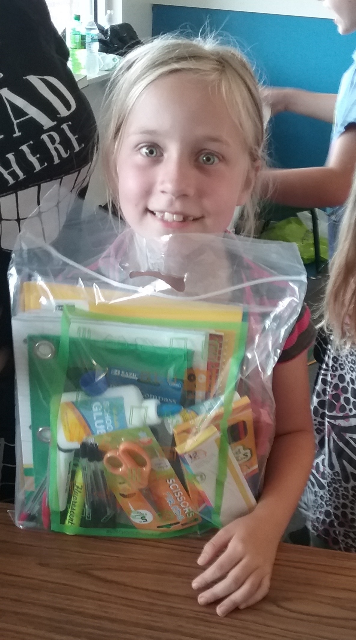 A young student in Georgia smiles while holding a clear backpack filled with school supplies for the new school year.
