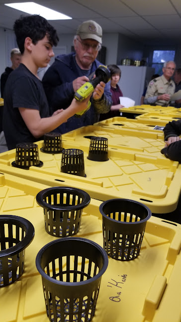 Youth and adult mentor drill openings in yellow tote lids to install net pots for hydroponic growing.