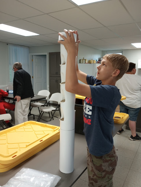 Middle school student stacks sections of PVC to build a vertical hydroponic tower