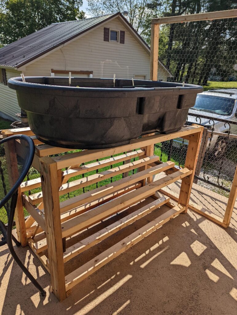 DIY hydroponic system on a wooden stand, with a large black tub set up on a porch for growing greens.
