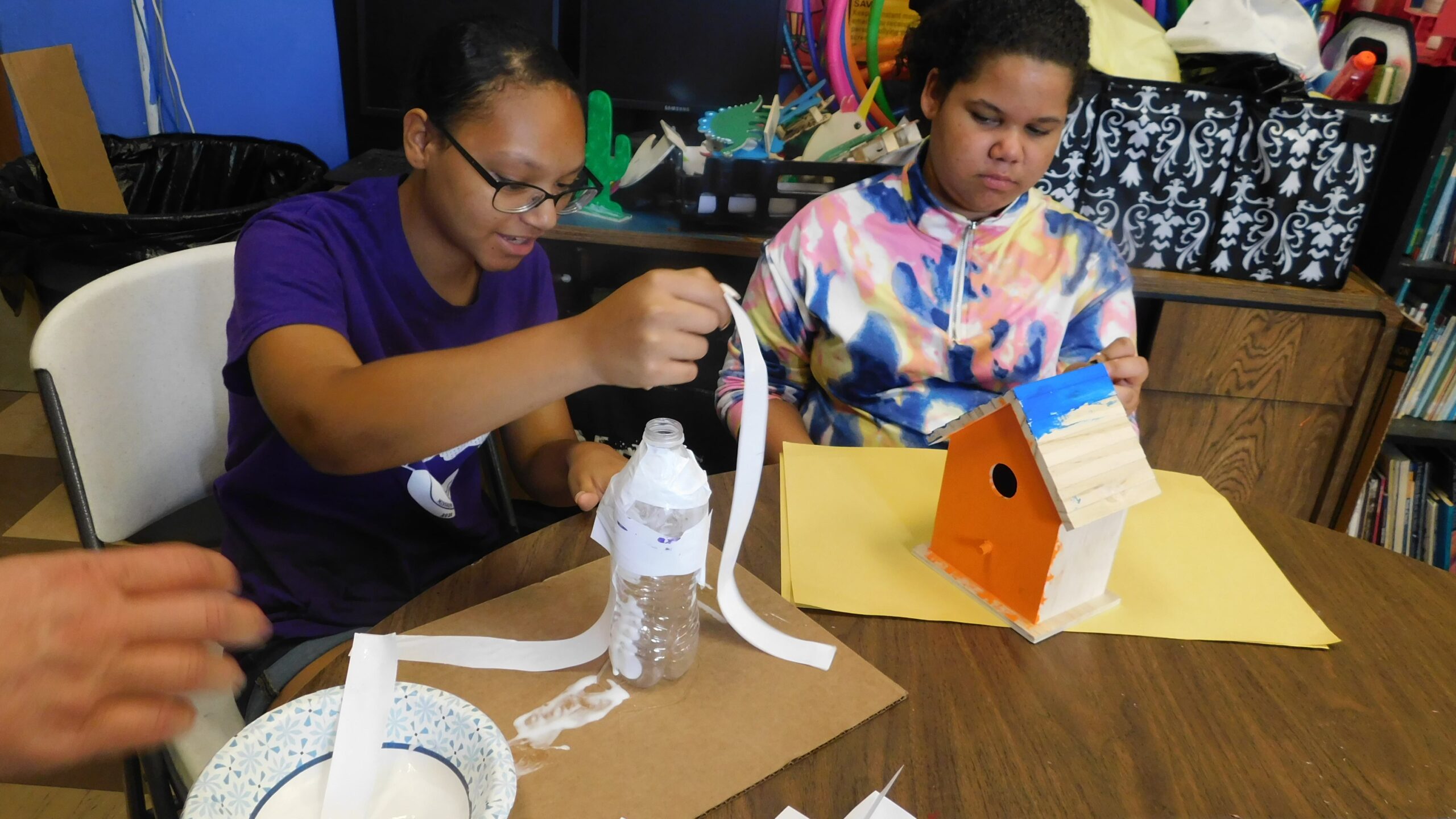 Girls painting a wooden birdhouse and building crafts during the Americans Helping Americans summer camp.