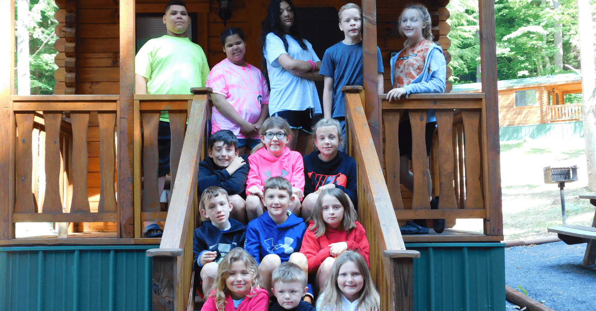 Summer Camps Give Appalachian Kids a Chance to Learn, Grow, and Have Fun A group of children and teens gathered on the steps of a cabin at a summer camp.