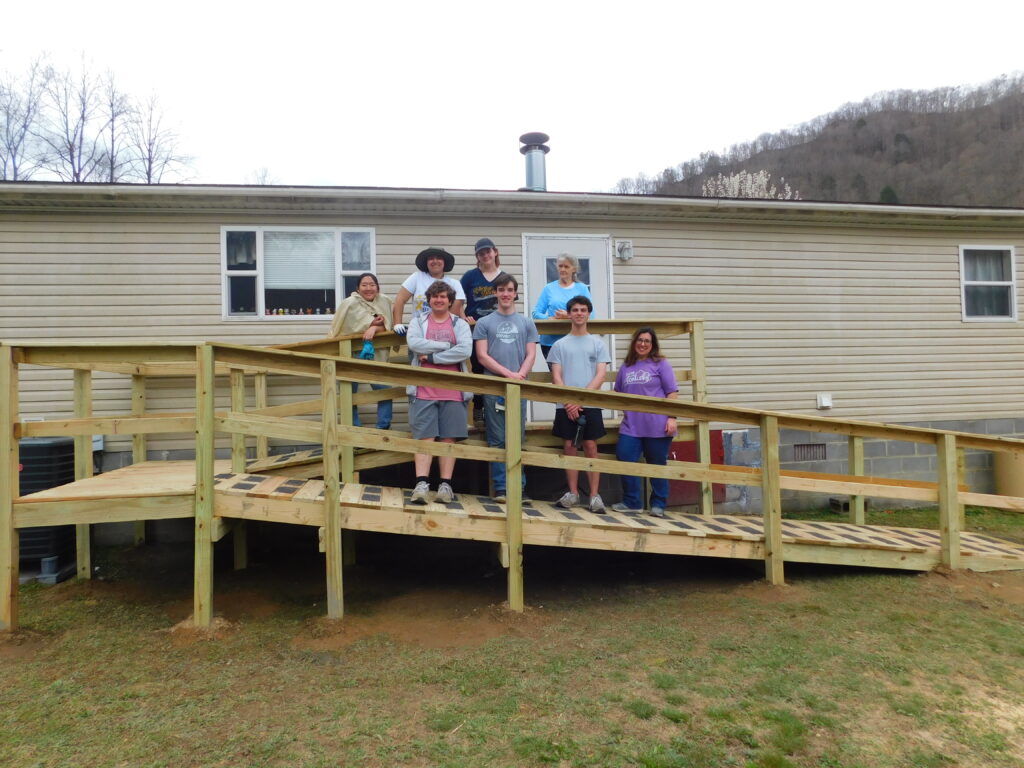 A group of dedicated volunteers stand on a newly completed handicap ramp for a family in rural East Tennessee.