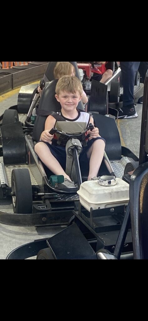 A young boy from McDowell County, WV, smiles while driving a go-kart during a community-partnered summer vacation.