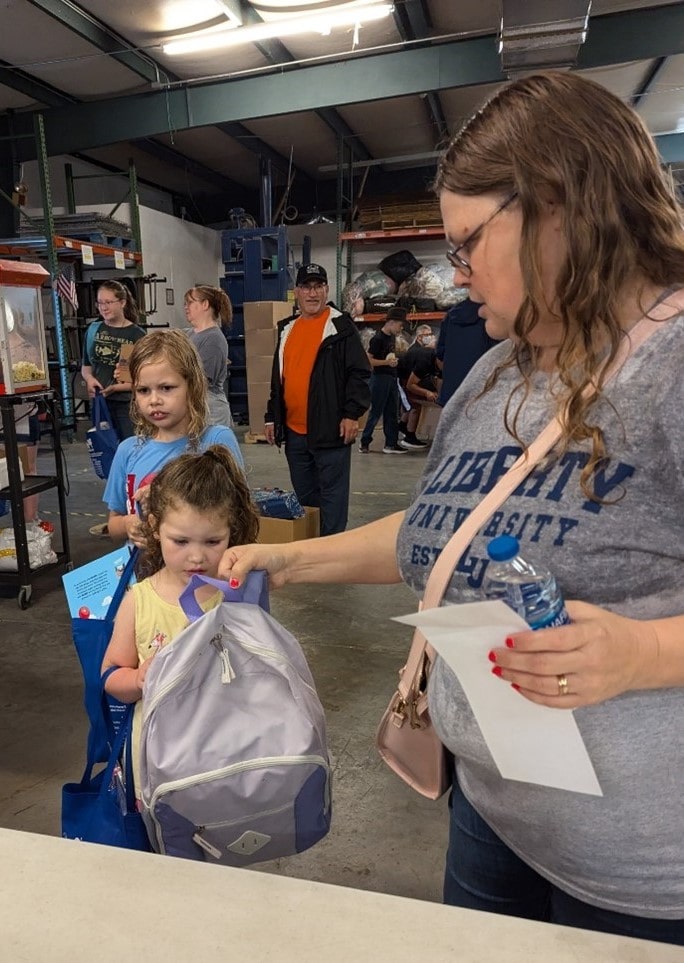 An AMOS partner helps a young girl in Tennessee try on her new backpack filled with school supplies.