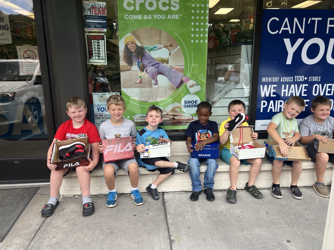 Group of boys sitting outside a shoe store showing their new shoes.