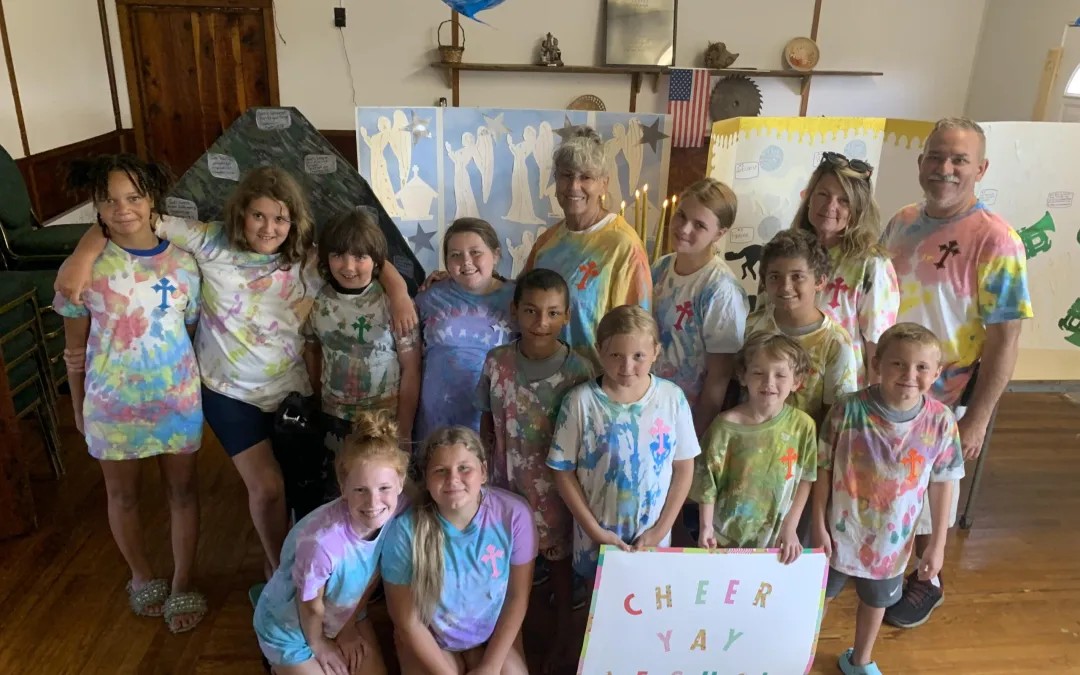 Children and adults in tie-dye shirts smiling during summer program.