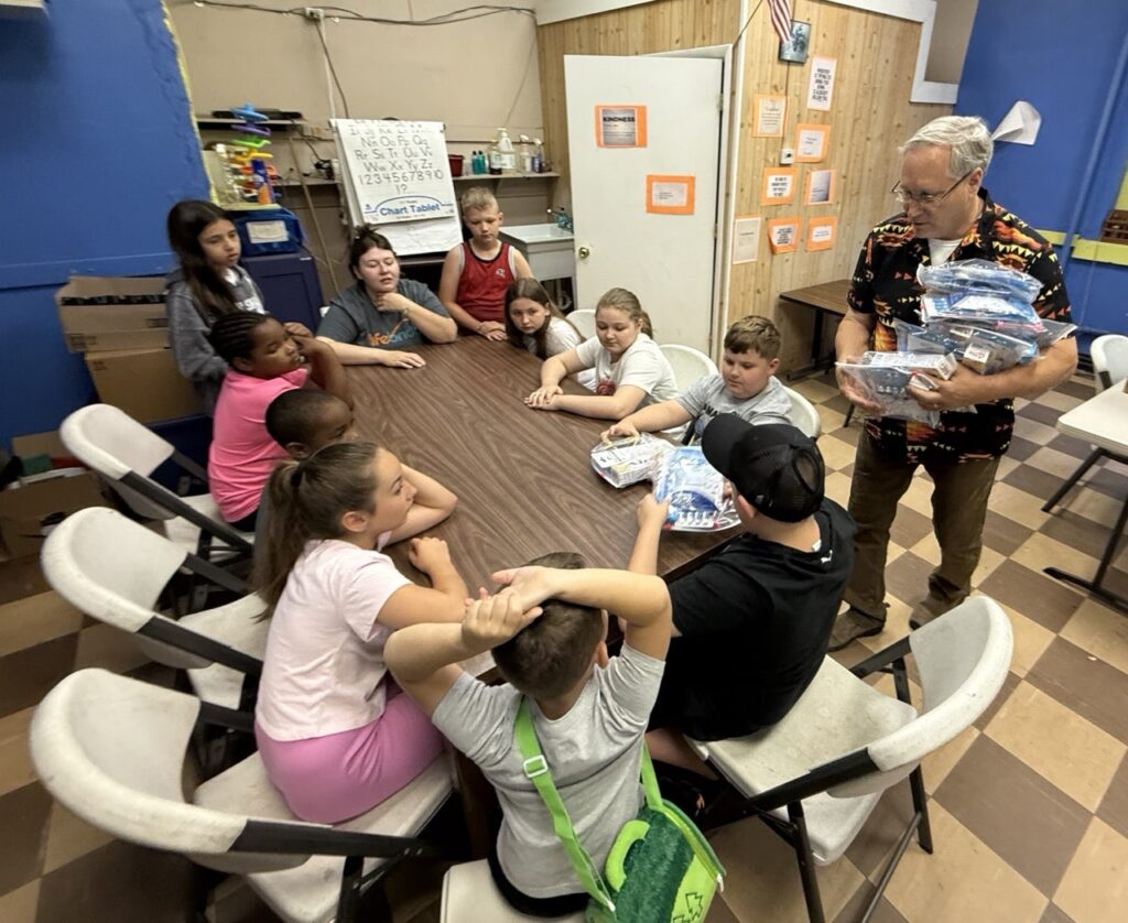BCPIA summer program kids around a table as staff hand out Americans Helping Americans Mighty Molars dental kits.