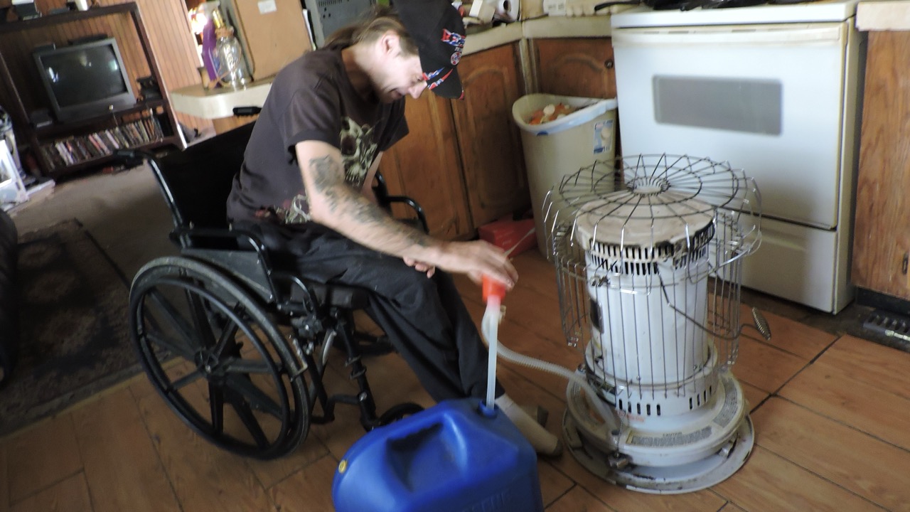 A man in a wheelchair refilling a kerosene heater inside his Appalachian home, supported through the Americans Helping Americans® utility assistance program.
