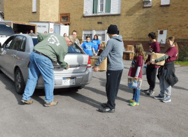 Volunteers loading food boxes into the trunk of a car during a community food drive to combat hunger in Appalachia.