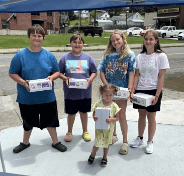 Group of smiling children and teenagers in Appalachia holding food boxes, benefiting from community support.