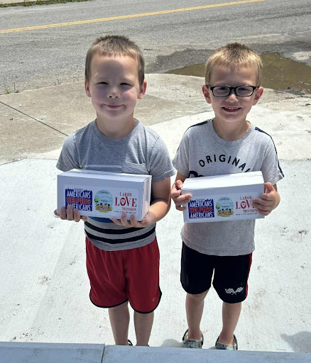 Two young boys smile while holding Americans Helping Americans food boxes.