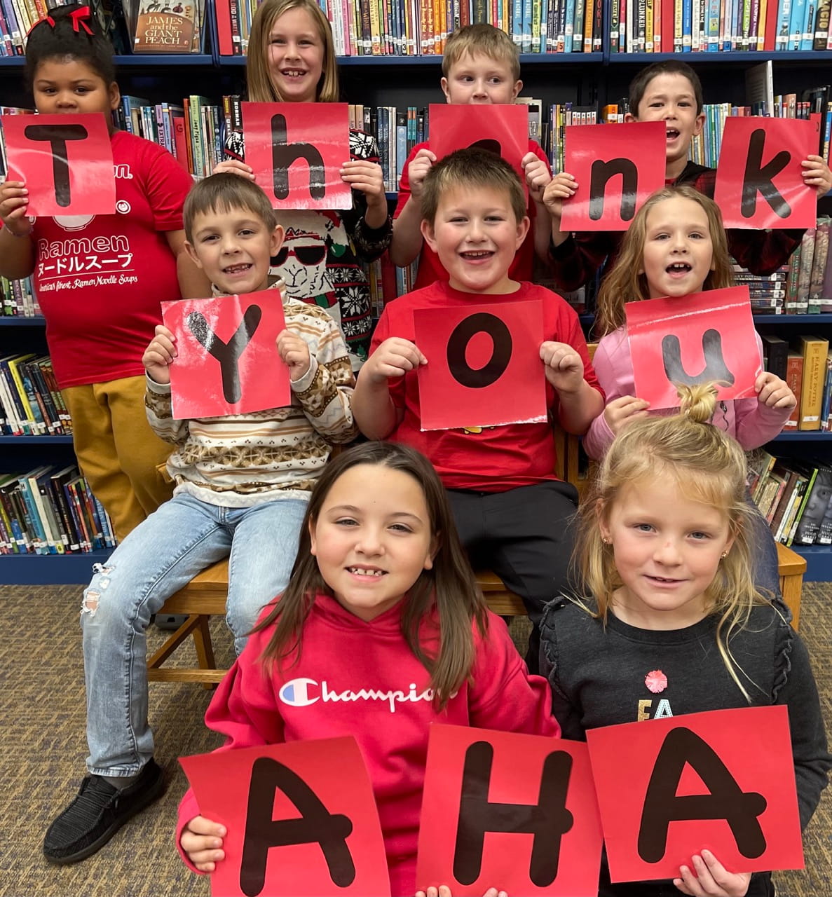 Students in a school library holding signs that spell Thank You AHA for Americans Helping Teachers grants